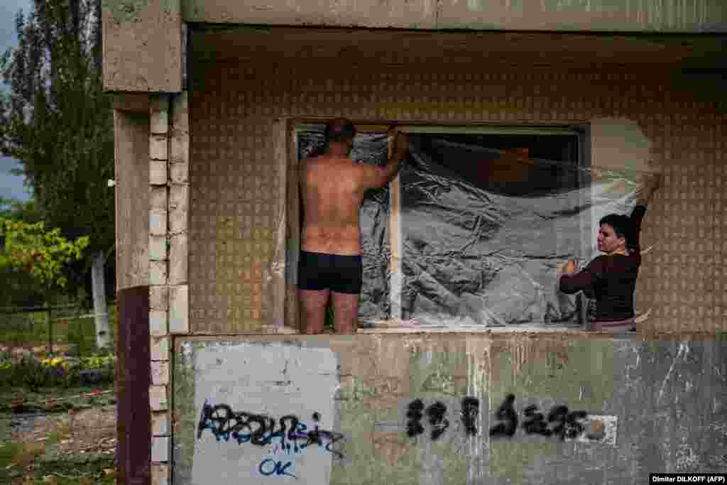 Javítanak, amit tudnak: helyi lakosok műanyag fóliával takarnak le egy betört ablakot a rakétacsapást követően