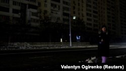 Жителка на Киев чака с кучето си на спирка на градския транспорт, потънала в мрак след руските обстрели в сряда.