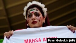 Иран футболчуларынын сүрөөнчүсү Тегеранда абакта каза болгон 22 жаштагы Махса Амининин ысымы жазылган футболканы кармап турат. Аминини полиция "хижаб салынуу эрежесин бузганы” үчүн кармап, кийин ал көз жумган. 