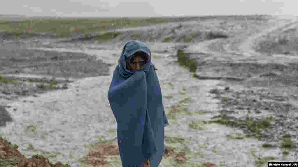 Një vajzë 9-vjeçare afgane mbulohet që të mbrohet nga një rrebesh shiu në fabrikën e tullave ku ajo punon.