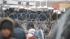 Мігранти на білорусько-польському кордоні перед парканом і польськими військовослужбовцями