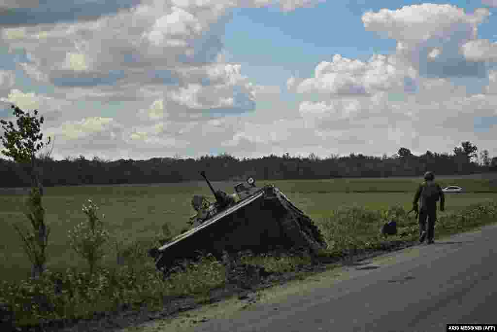 Një ushtarak ukrainas duke kaluar pranë një automjeti të blinduar ukrainas të dëmtuar.