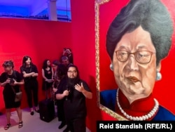 Badiucao kínai művész (az előtérben) a prágai Dox Kortárs Művészeti Központban rendezett kiállításon a Carrie Lam–Hszi Csin-ping-képpel 2022. május 12-én