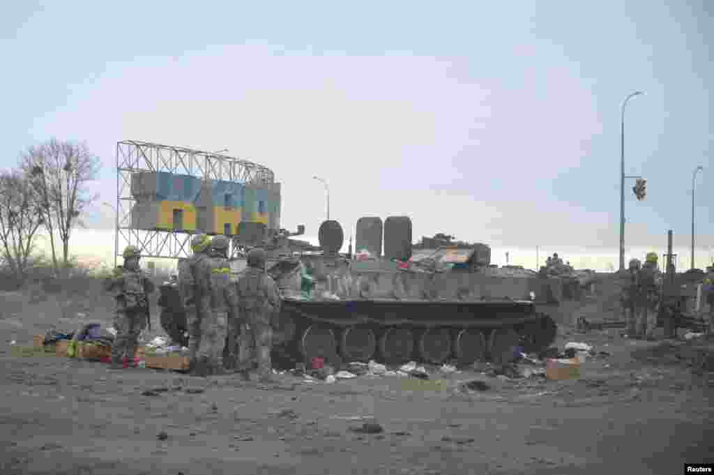 Ukrán katonák egy elpusztított katonai jármű mellett Harkov külvárosában február 25-én