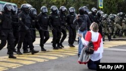 Беларус желегин жамынган аял полиция кызматкерлеринен күч колдонбоону өтүнүүдө. Минск. Сентябрь, 2020-жыл.