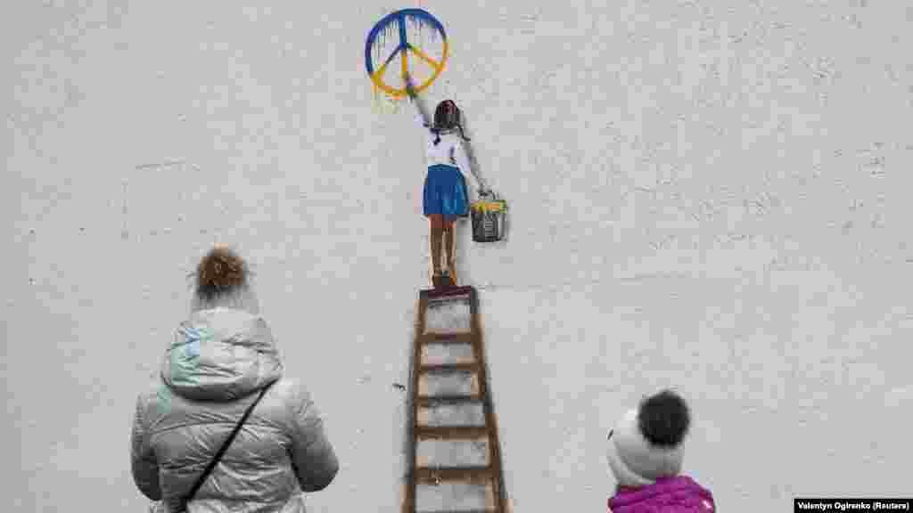 O femeie și un copil privesc pictura murală a lui Tvboy pe peretele unei școli din Bucea care înfățișează o fată pictând un simbol al păcii Exponent al mișcării&nbsp;italiene Neopop, Tvboy a scris despre experiența sa: &bdquo;Doar vizitând Ucraina am înțeles cu adevărat&nbsp;puterea și vitejia acestui popor&rdquo;.