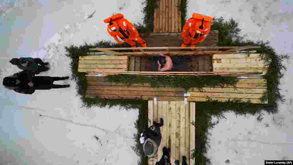 Mii de ortodocși s-au scăldat în rîuri, iazuri sau copci, cum au făcut acești oameni sub privirile a doi salvatori la Kronstadt, lângă St. Petersburg, Rusia, pe 18 ianuarie. &nbsp;