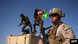 Në këtë fotografi të bërë më 28 gusht 2017, një marins amerikan shikon teksa ushtarët e Ushtrisë Kombëtare Afgane ngrenë flamurin kombëtar afgan në një automjet të armatosur gjatë një stërvitje.