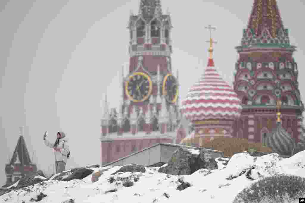 Женщина делает селфи в парке "Зарядье" на фоне Спасской башни Кремля и собора Василия Блаженного после снегопада в Москве 7 апреля 2025 года. AP Photo/Pavel Bednyakov