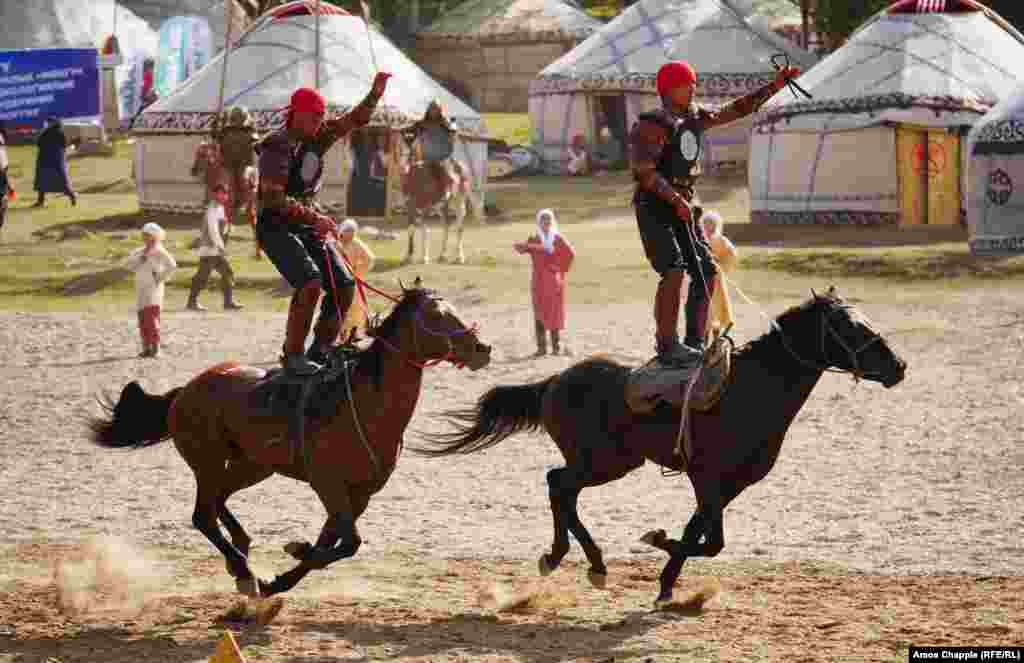 Riders stand atop their horses as they speed past the crowds.