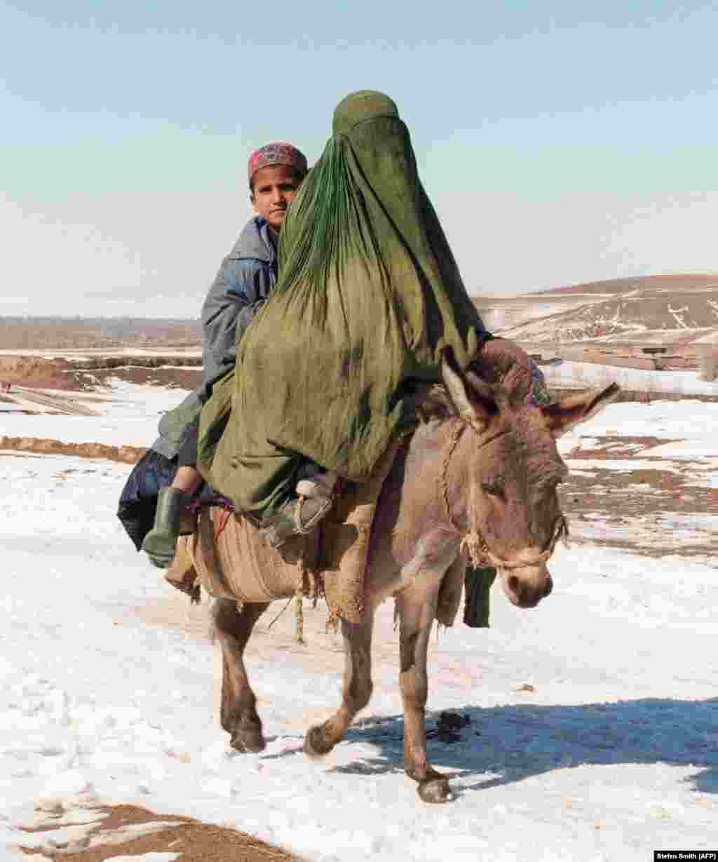 Un băiat și o femeie acoperită cu un voal călăresc un măgar. În conformitate cu regulile talibanilor, femeile erau obligate să poarte un asemenea voal când erau în afara casei și puteau să-și părăsească locuința doar acompaniate de o rudă de sex masculin.