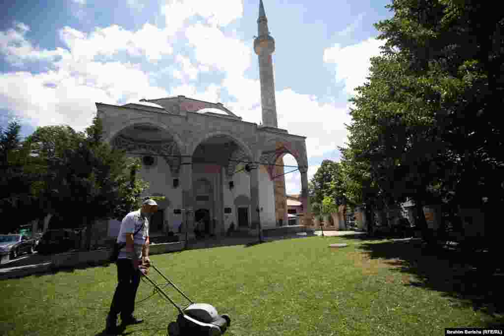 Чоловік косить траву в саду Великої мечеті в столиці Косова Приштині