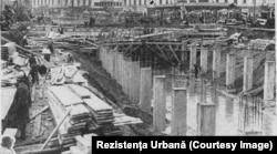 c. 1932-1933. Stâlpii planșeului Dâmboviței la intrarea în Piața Unirii. În fundal se văd Strada Halelor și Hanul lui Manuc.