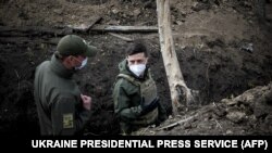 Volodimir Zelenszkij ukrán elnök egy tiszt társaságában sétál egy lövészárokban. Az elnök a donyecki régióban fekvő Petrivszke falu közelében állomásozó ukrán katonai egységhez látogatott el, 2020. április 11-én.