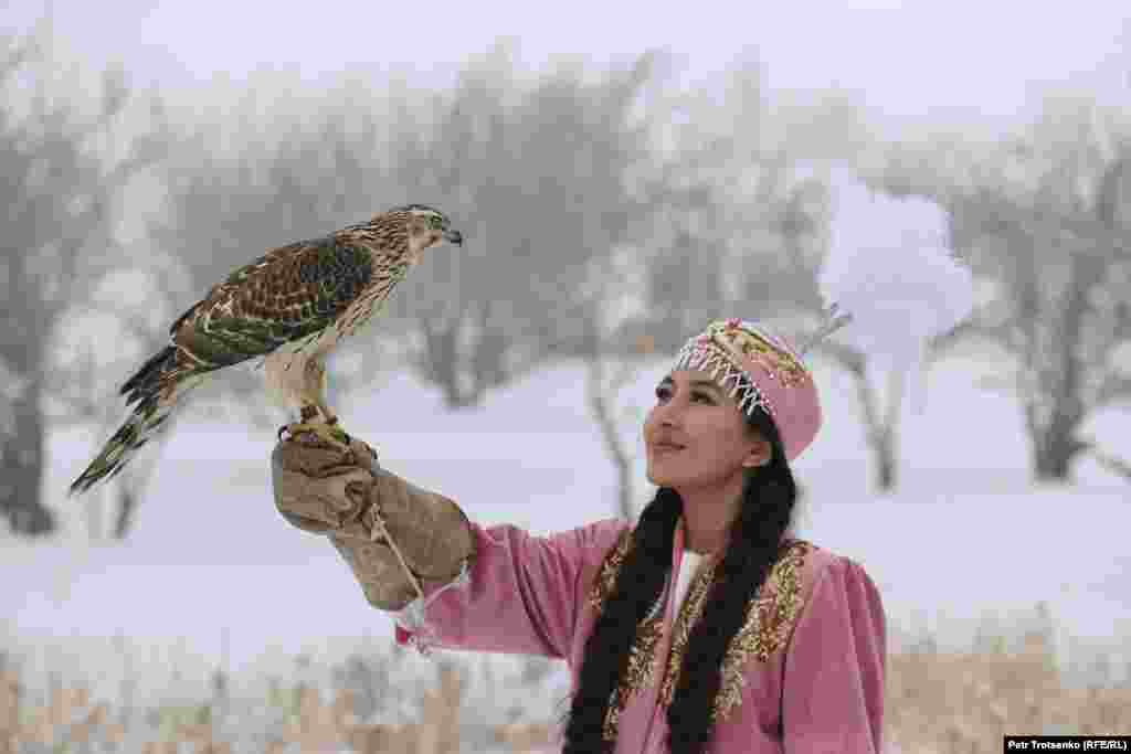 Девушка в национальном наряде держит на руке хищную птицу.