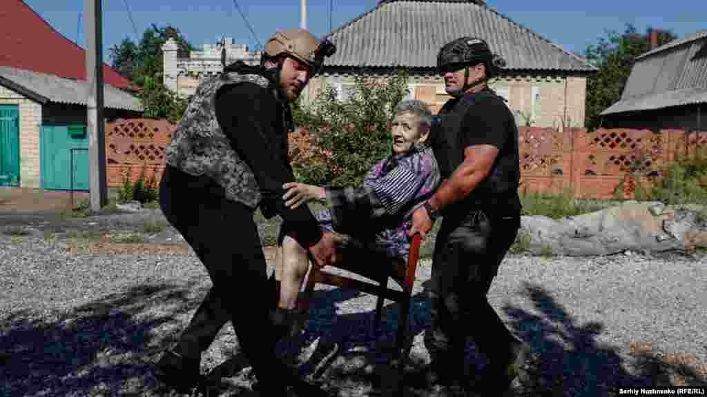 Egy idős asszony evakuálása a donyecki Novohrodivkából 2024 augusztusában. Az orosz csapatok húsz nappal a kép készítése után elfoglalták a várost. A jobb oldali férfi Owen, egy új-zélandi önkéntes, aki korábban katonaorvos volt