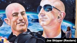 Маргарита Моилина од Ел Пасо, Тексас, позира покрај муралот кој ги прикажува американскиот милијардер бизнисмен Џеф Безос и неговиот брат Марк (Л) еден ден пред нивното лансирање на инаугуративниот лет на Blue Origin до работ на вселената