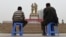 China - TO GO WITH CHINA-XINJIANG-UNREST-MIGRATION-POPULATION BY BENJAMIN HAAS This photo taken on April 16, 2015 shows a Uighur man and boy watching a performance under a statue of late communist leader Mao Zedong meeting with a Uighur, in the central 