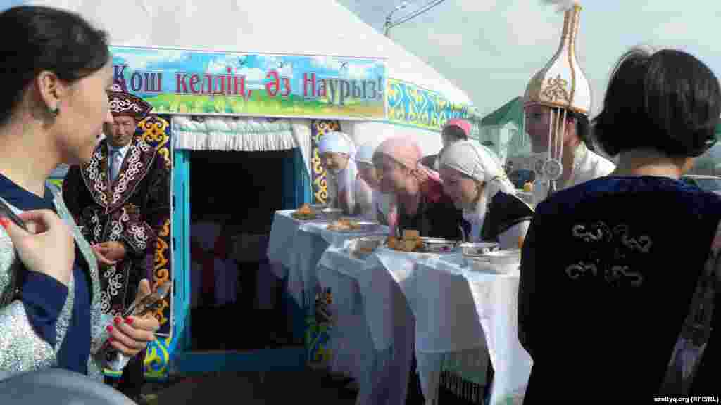 Женщины у юрты приветствуют гостей, предлагая отведать угощения.&nbsp;