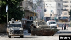 Žena s djecom pored vozila hitne pomoći dok izraelska vojna vozila prolaze tokom racije, u Jeninu, na Zapadnoj obali pod izraelskom okupacijom 14. decembra 2023.