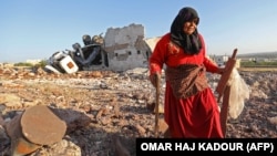 تصویر زنی که در حال جمع‌آوری بقایای اثاث خانه‌اش در ادلب پس از حملات هوایی است