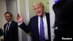 دونالد ترامپ در حالی که مایک والتز در کنار او ایستاده به سوالات خبرنگاران در هواپیمای ریاست جمهوری پاسخ می‌دهد