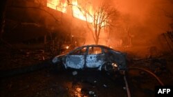 A burnt car is pictured in front of a burning house following a Russian drone strike in Kharkiv, Ukraine, on June 11.