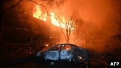 Un automobil incendiat este surprins în fața unei case în flăcări, după un atac cu dronă rusă la Harkov, pe 11 iunie 2025, în contextul invaziei ruse în Ucraina.