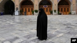 زنی با چادر کامل و سیاه‌پوش، در حیاط یک مسجد نماز می‌خواند