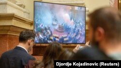 Gazetarët duke shikuar transmetimin e drejtëpërdrejtë të seancës plenare, teksa deputetët opozitarë serbë hedhin bomba tymuese. 4 mars 2025. 