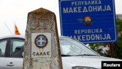 A car travels past a Greek border stone and a sign on the border of Macedonia and Greece.