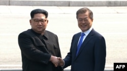 Кадр із відео корейського телебачення: північнокорейських лідер Кім Чен Ин і президент Південної Кореї Мун Чже Ін тиснуть руки біля демаркаційної лінії, що розділяє держави, 27 квітня 2018 року