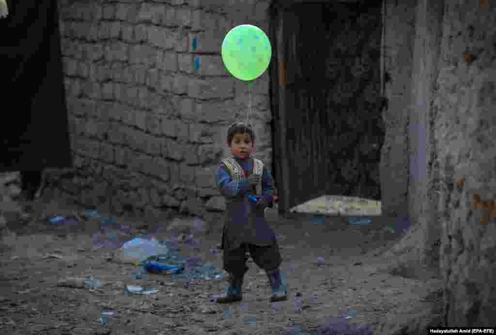 Një djal afgan mban në duar një tullumbace teksa qëndron pranë një strehe të përkohshme në periferi të Kabulit, ku janë të strehuar qytetarët që janë shpërngulur nga shtëpitë e tyre. (epa-EFE/Hedayatullah Amid)