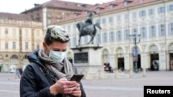 Көчөдө телефонун тиктеп бараткан аял. Иллюстрациялык сүрөт. Италиянын Турин шаарында тартылган.