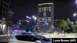 Mașină de poliție în centrul orașului Milano, nordul Italiei. Pe fundal, clădire a administrației pe care scrie „Stați acasă!”