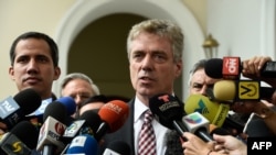 دانیل کرینر، سفیر آلمان در ونزوئلا، در حال گفت‌وگو با خبرنگاران. خوان گوایدو، رهبر مخالفان و رقیب مادور، نیز در تصویر دیده می‌شود.