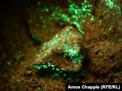 تکه‌سنگ‌هایی با لکه‌های مواد رادیواکتیو داخل یک معدن متروکه اورانیوم مربوط به دوران شوروی. این کانی‌ها زیر پرتو چراغ‌های ماوراء بنفش مخصوص شناسایی مواد رادیواکتیو می‌درخشند.