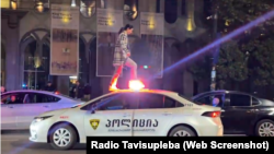 Aksiyaçılardan biri polis maşınının üstünə çıxıb.