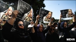 Women hold pictures of Iranian poet Simin Behbahani at her funeral in Tehran on August 22.