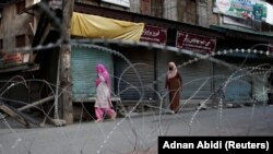 Kashmiri women walk past concertina wire laid across a road during restrictions after the scrapping of the special constitutional status for Kashmir by the Indian government in Srinagar on August 20. 