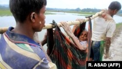 Бангладешке качкан рохинжа мусулмандары карыган кемпирди көтөрүп баратышат. 3-сентябрь, 2017-жыл
