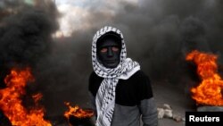 Палестинський демонстрант стоїть біля палаючих шин під час сутичок з ізраїльськими військами