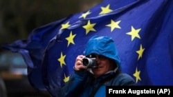 Un trecător fotografiază protestatarii anti Brexit în fața clădirii Parlamentului din Londra
