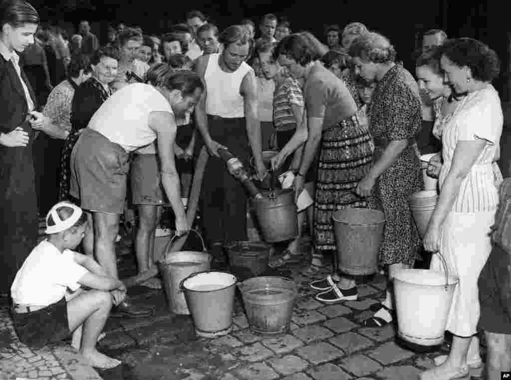 Berlinezi din Berlinul de Vest așteaptă să își umple gălețile de apă la un hidrant, pe 3 iulie 1948. După ce sovieticii au întrerupt aprovizionarea cu apă, locuitorii erau nevoiți să stea la coadă ore în șir.
