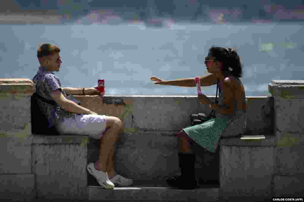 Двајца млади се освежуваат со пијалоци и сладолед покрај реката Тахо, во Лисабон, на 29 јуни.