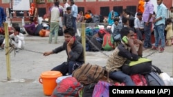 Indian migrant laborers speak on their mobile phones as they prepare to leave the region, at a railway station in Jammu, on August 7.