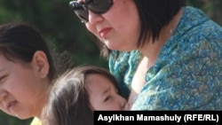 Жеңіс күніне арналған мерекелік шараны тамашалауға келген әйел баласын емізіп отыр. Ақтау, 9 мамыр 2012 жыл.