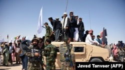 FILE: Afghan Taliban militants and residents stand on a armored Humvee vehicle of the Afghan National Army (ANA) as they celebrate a ceasefire on the third day of Eid in Maiwand district of Kandahar Province in June 2018.