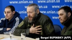 Киевдеги басма сөз жыйынында орусиялык аскер туткундары, полиция кызматкери (сол жакта) сержант Евгений Плотников, полиция офицерлери подполковник Дмитрий Астахов жана капитан Евгений Спиридонов. 