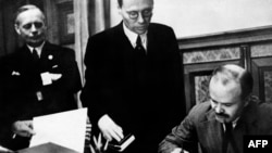 Viaceslav Molotov semnează, iar Joachim von Ribbentrop îl flanchează la semnarea pactului de neagresiune între Germania nazistă și URSS, 23 august 1939, Moscova.